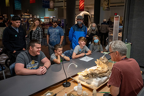 exhibit visitors talk with a volunteer about the fossil they are working on