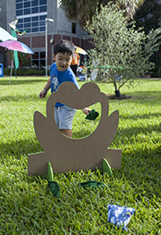 child throwing beanbag through frog cut-out