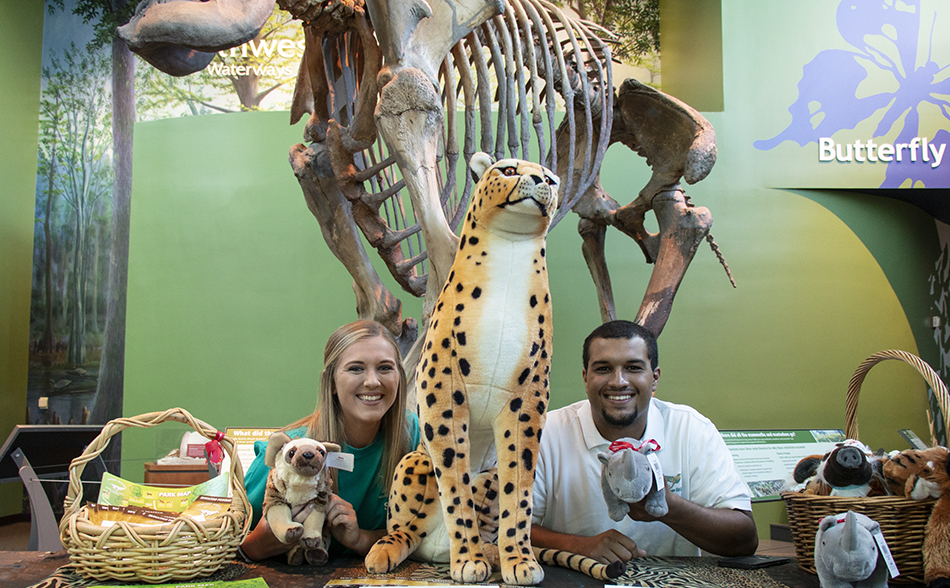 People at table with plush animals in front of mammoth fossil