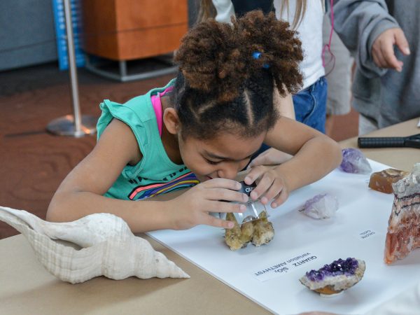 young girl looks through a magnifier at a quartz