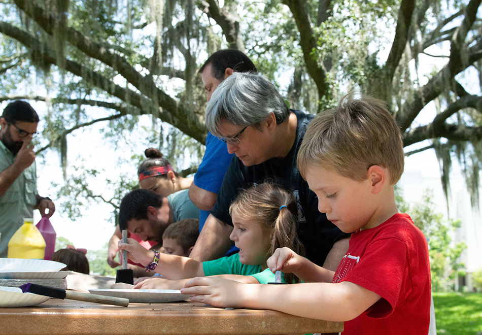 group of children and adults working of craft projects on a picnic table outside