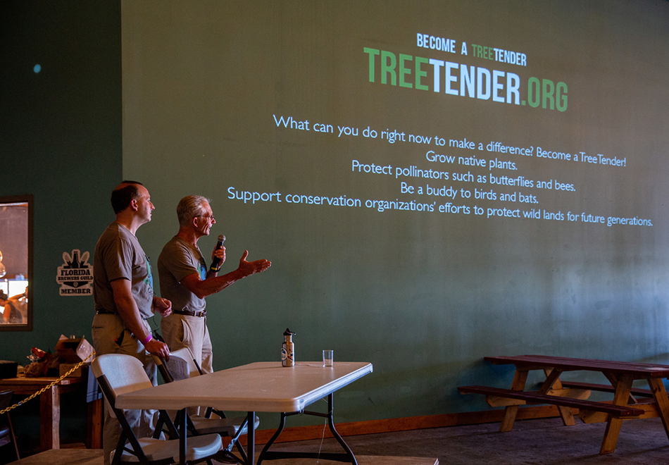 two presenters are standing next to a projection screen showing a title slide for TreeTender Org