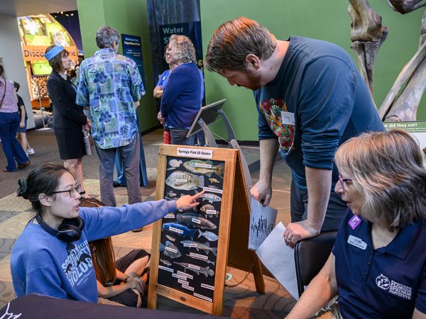 a person is kneeling and pointing at fish stickers on a board to 2 people