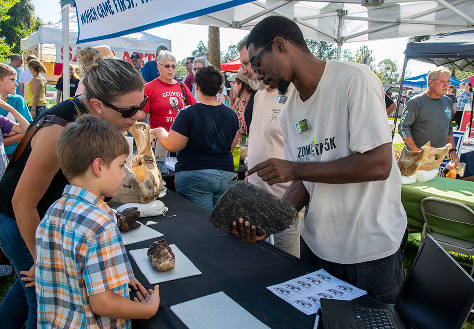 a person is holding a large fossil of some kind so a child and an adult can get a close view at an outdoors event