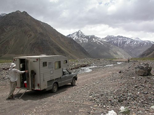 camper truck on an unpaved moutain road with snowcapped mountains in the background