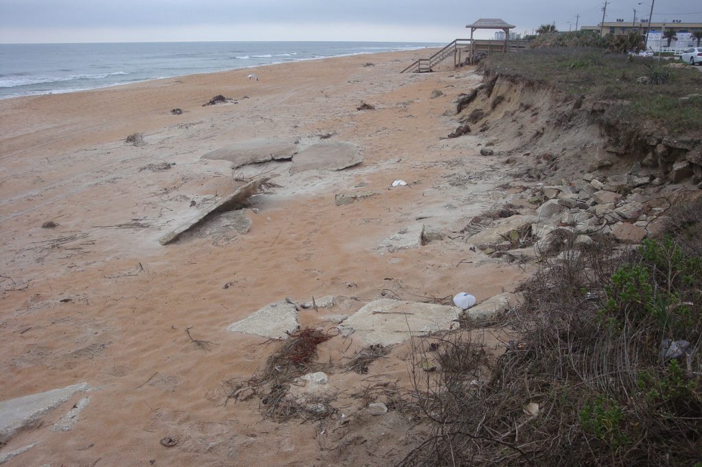 large concrete slabs sit mostly submerged in the sand along the coastline