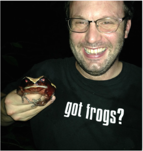person smiling and holding a large frog. His shirt reads got frogs?