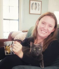 person holding a mug and smiling. A cat sits in her lap