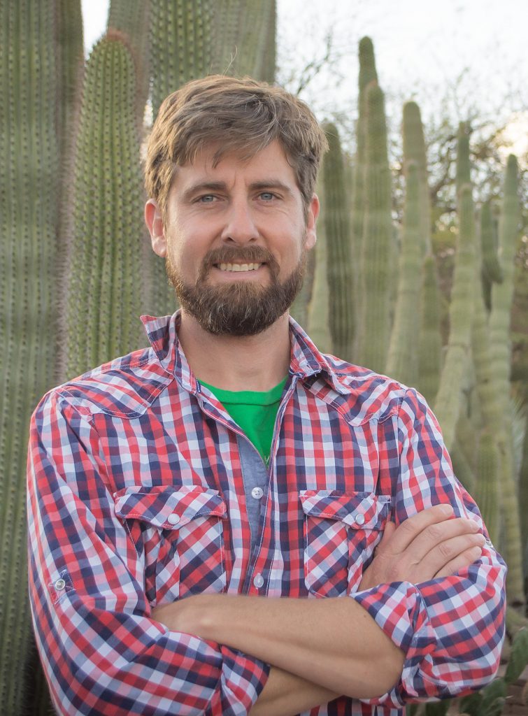 Lucas Majure standing in front of tall cactus plants, arms crossed