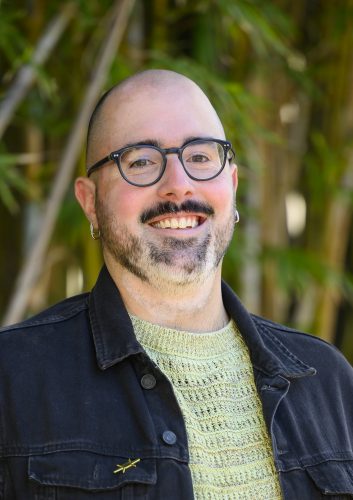 A photo of a person with glasses and a beard smiling towards the camera.