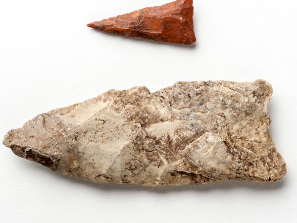 two Projectile Points showing the size difference. One is small red triangle with a long sharp point, the other is many times larger, one end squared off the other end sharpened to a point