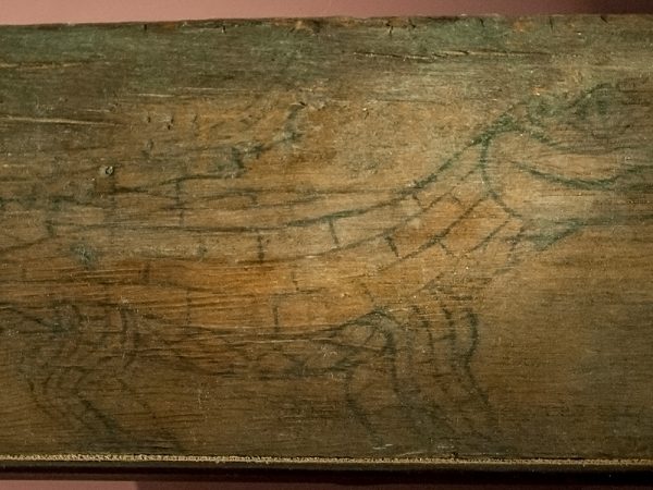 Flat piece of wood displayed and lit to show a faint line drawing of an alligator