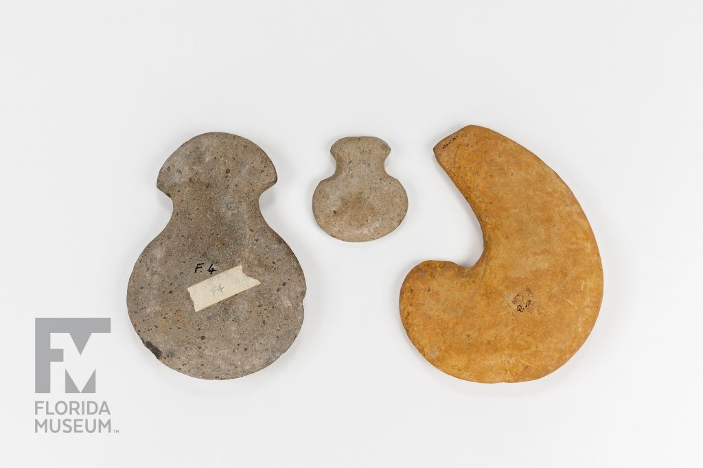 three stone hoes of various sizes, shapes, and color. Each has a wide semicircular base and a sharper tip.