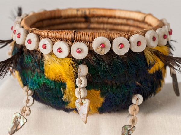 coiled basket decorated with bright yellow and blue-green feathers, shells and beads.