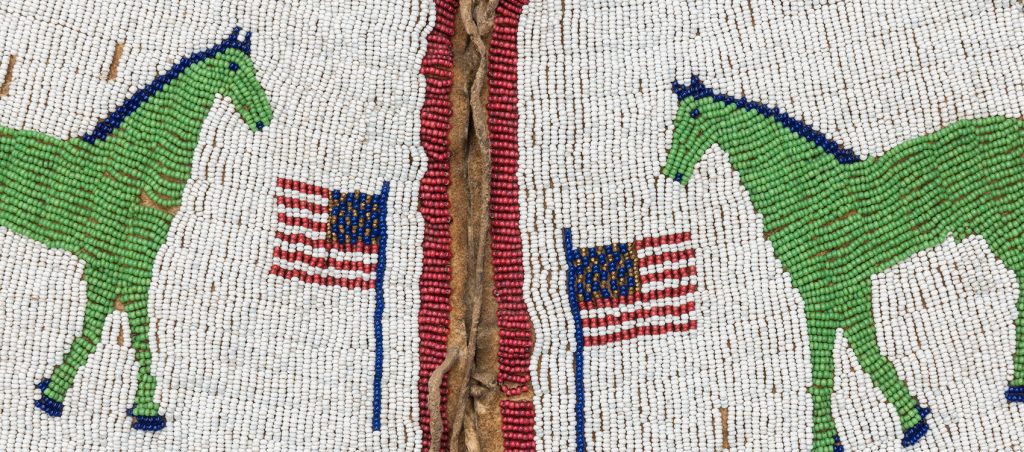 Close up of the beaded vest to show the rows of tiny seed beads sewn to create two green and blue horses and two American Flags in red, white, blue and gold, all against a background of white created by even more seed beads