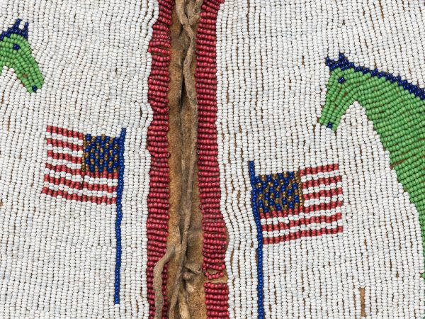Close up of the beaded vest to show the rows of tiny seed beads sewn to create two green and blue horses and two American Flags in red, white, blue and gold, all against a background of white created by even more seed beads
