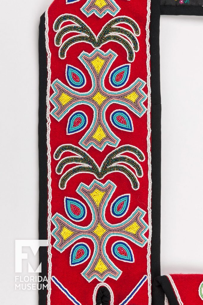 The shoulder strap of a Seminole Shoulder Bag made from red fabric and heavily decorated with seed bead designs