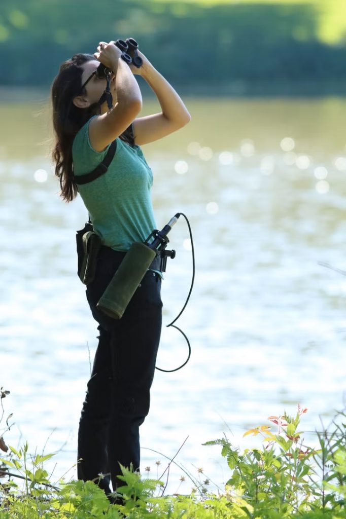 researcher using binoculars white standing next to a river