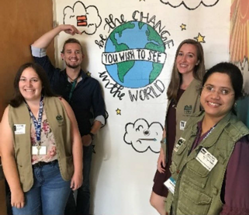 four volunteers in vests stand in front of a banner with a positive school message