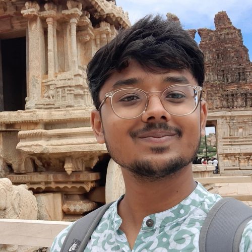 A photo of a person smiling towards the camera and wearing glasses.