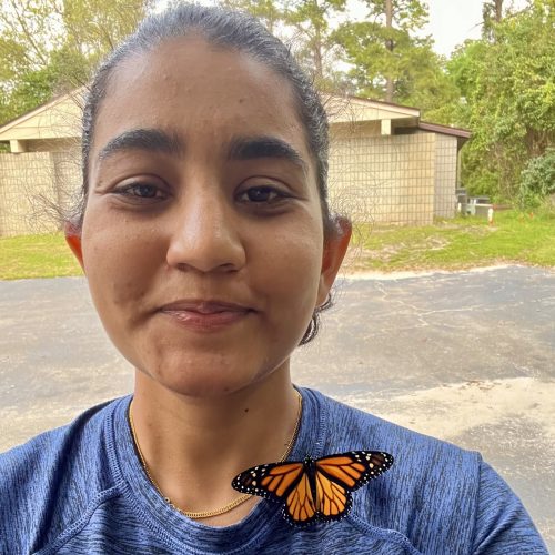 A photo of a woman outdoors with an orange butterfly on her.