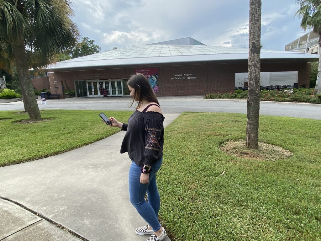 Person looking at phone, the Florida Museum can be seen behind her