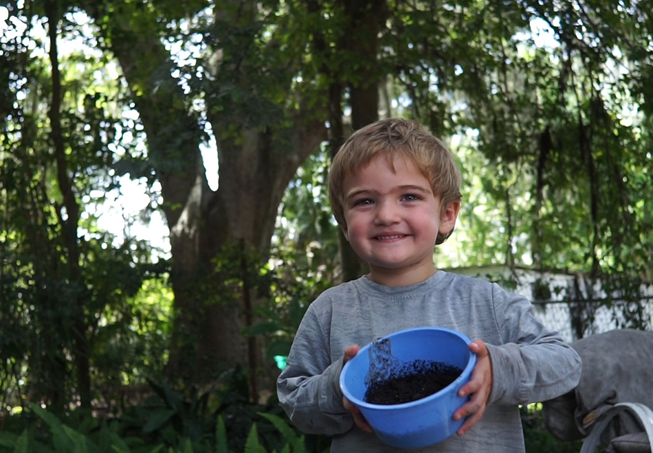 Child holding a blue bucker filled with dirt