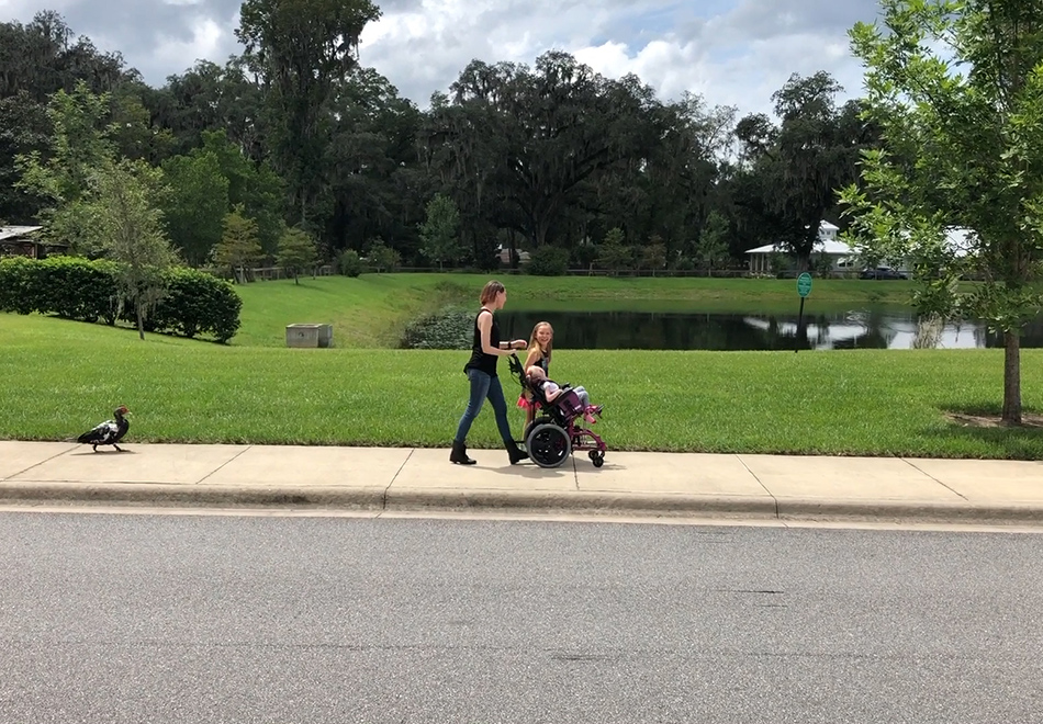 An adult and two children, one in a wheelchair, walking on a side walk