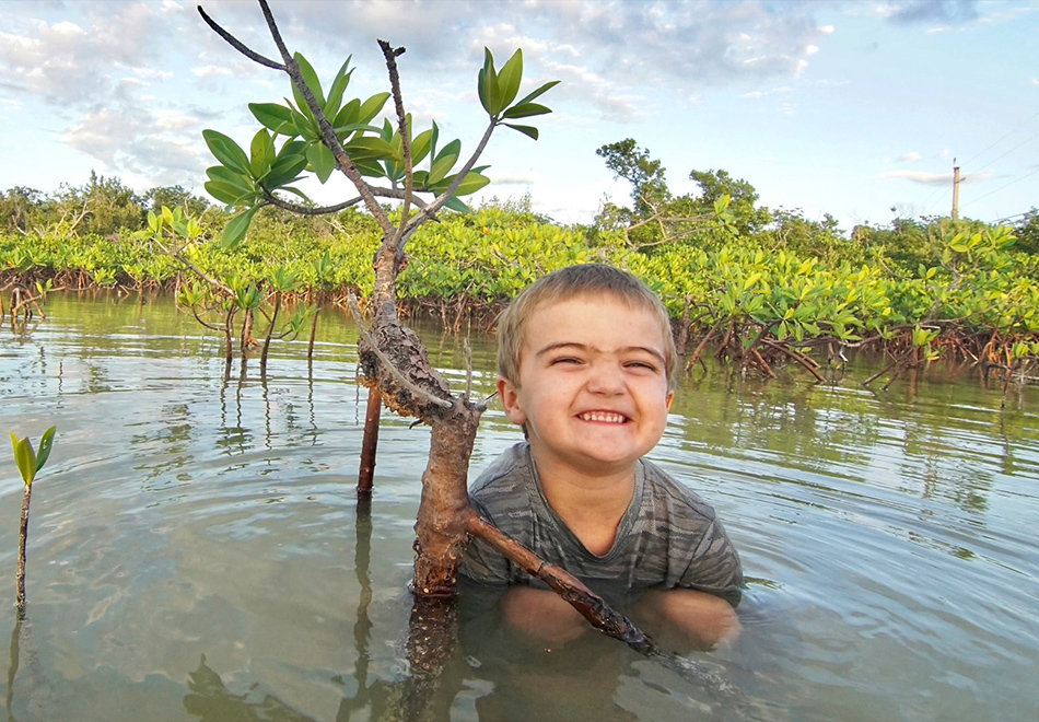 young child sitting in a shallow pond and smiling