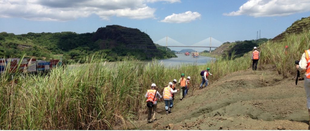 people in safety vests and hard hats waling along a canal