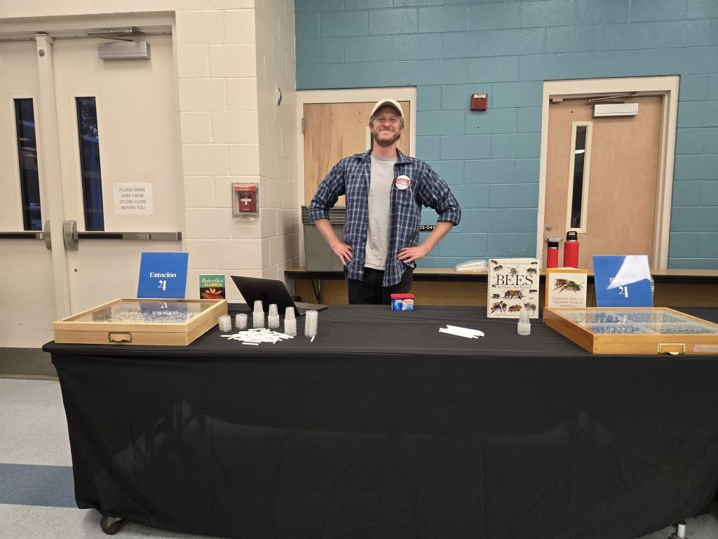 A people behind a table set with information about insects, drawers on insect specimens and supplies to build a bug catcher