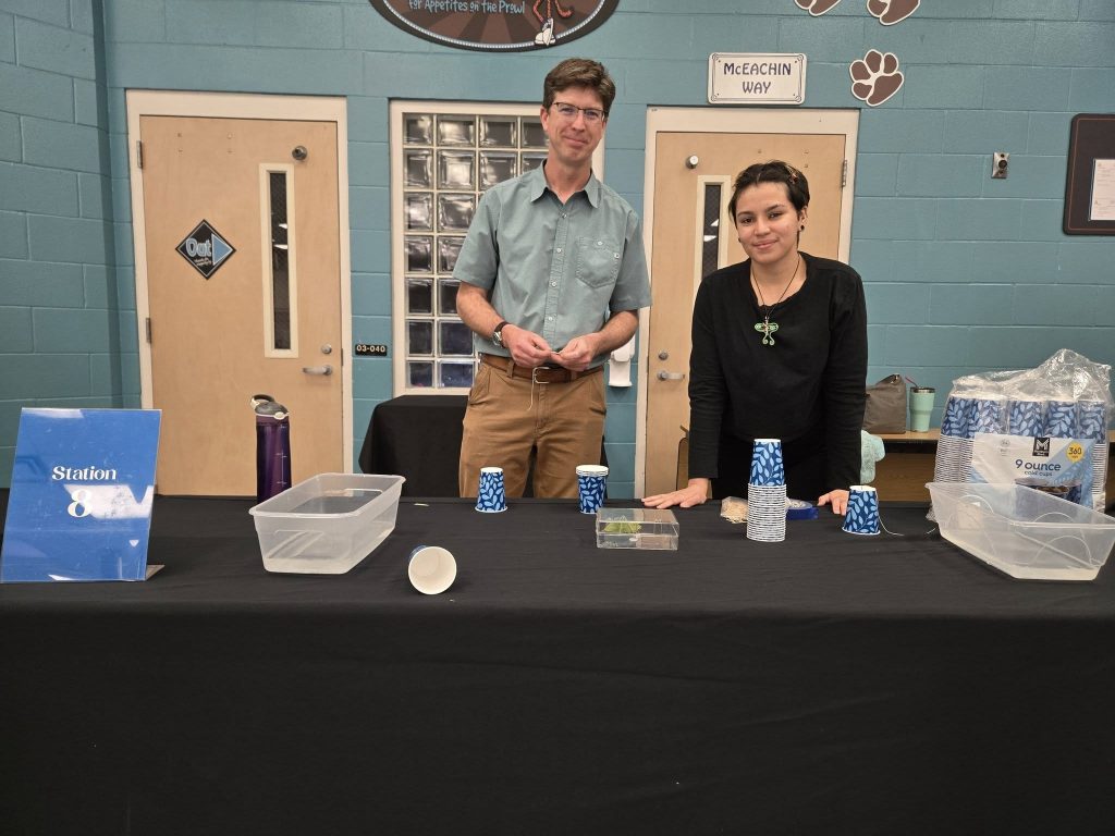 Two people behind a table with trays of water, cups and string