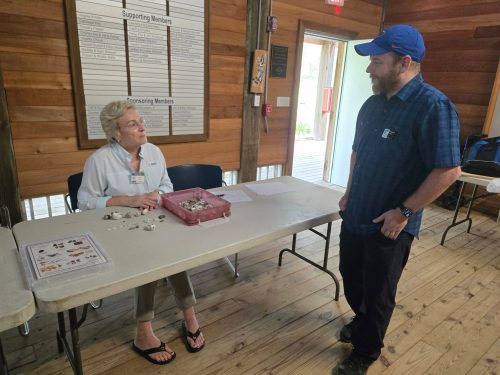 Alberto López speaks to a volunteer seated at a table with a collection of shells and an identification guide set in front of her