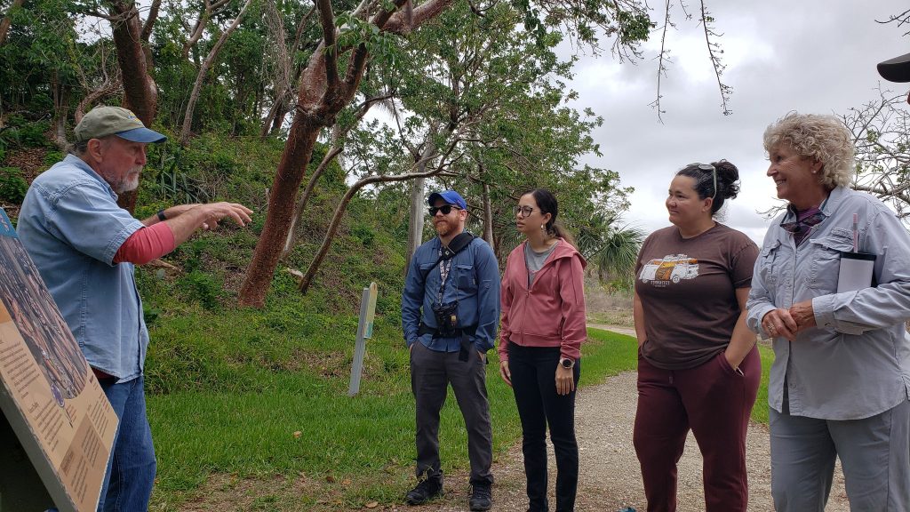 a group of people on a gravel pathway listen to a tour guide