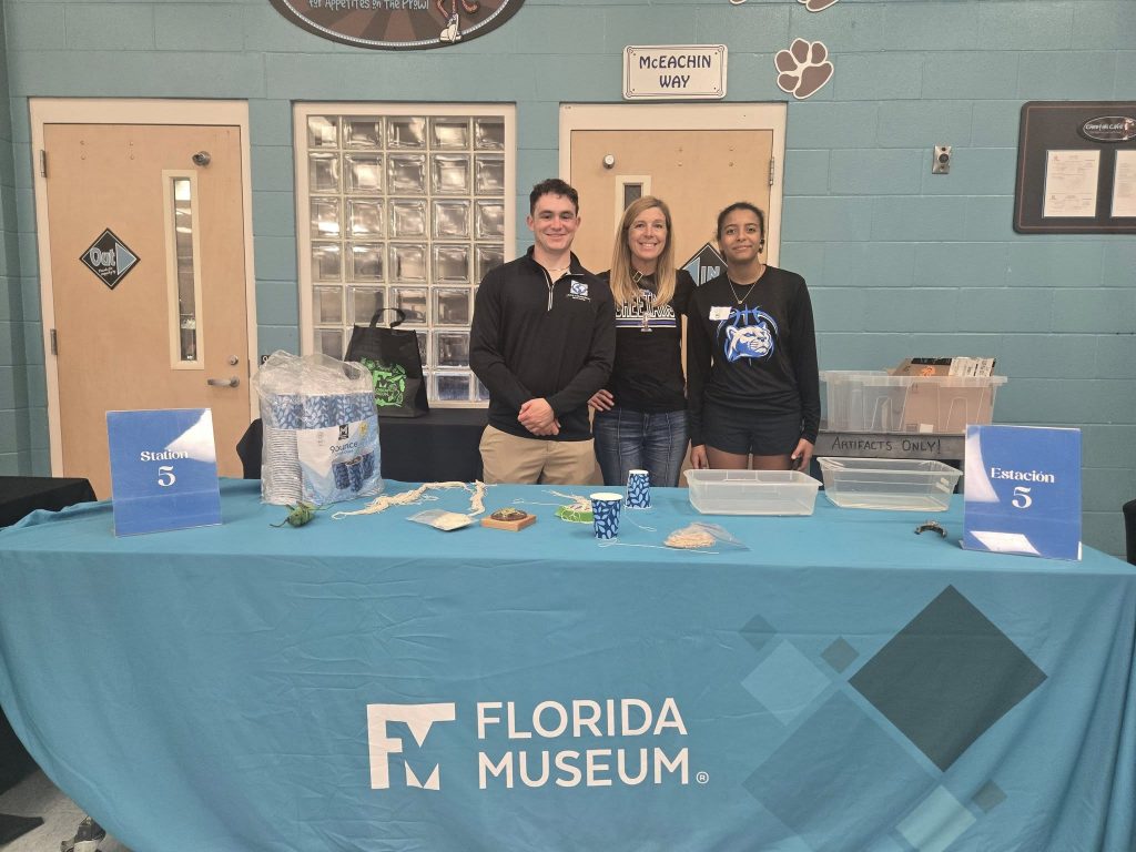 three people standing behind the station 5 table set with items for a science activity