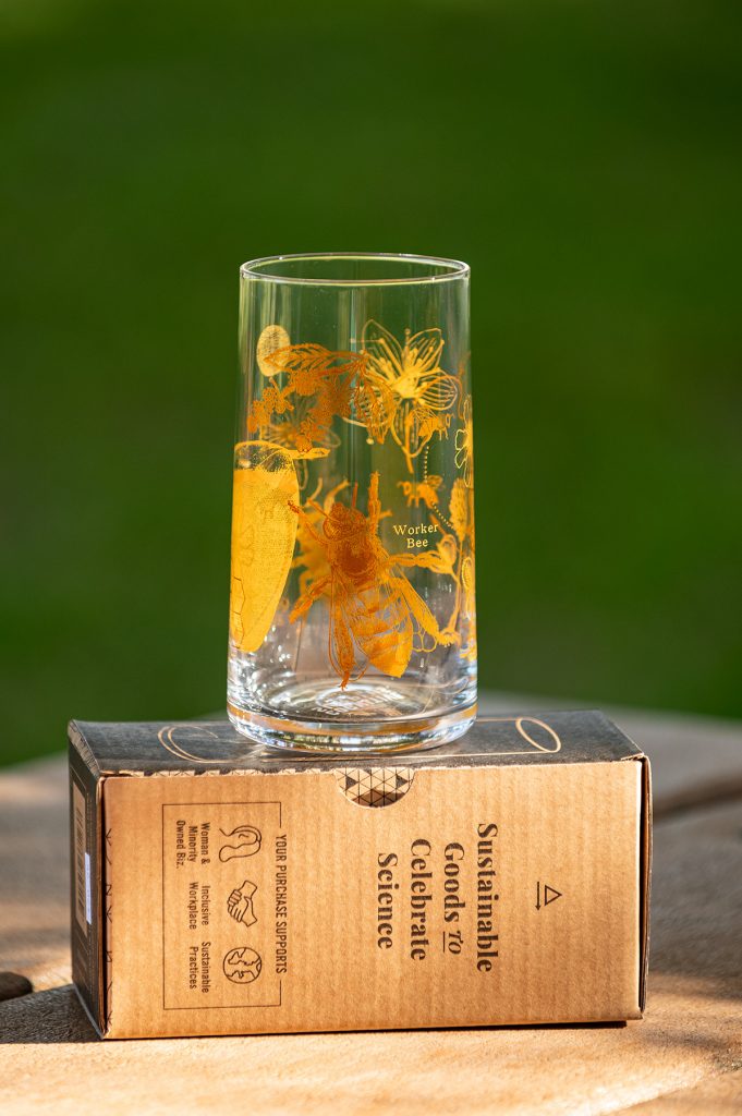 a glass printed with images of various bugs in yellow ink sitting on the glass' packaging