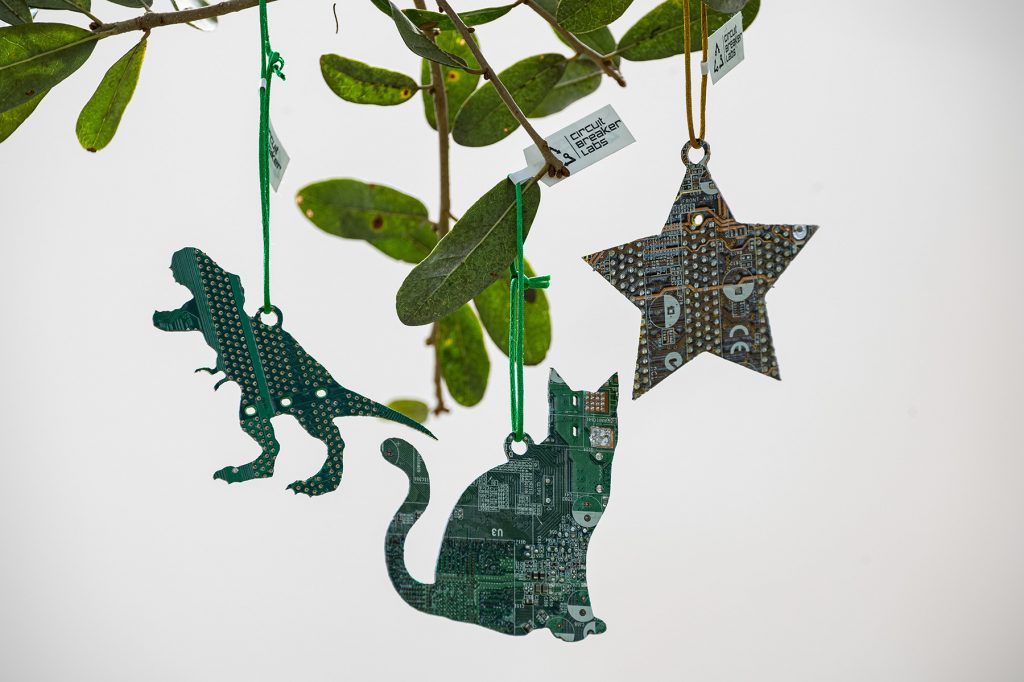 three ornaments made from circuit boards, shaped like a star, cat, and t-rex