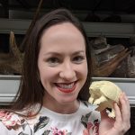 Rachel Narducci in front of shelves with fossils holding an armadillo model