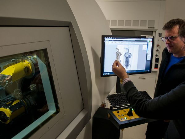 two reseachers stand next to CT scanner and look at computer screen, one is holding a 3-D printed replica of a frog