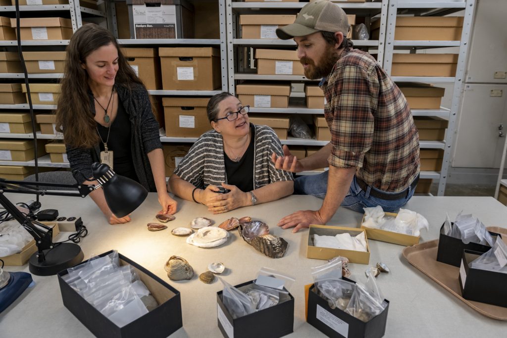 three scientists examine table covered in mussel shells