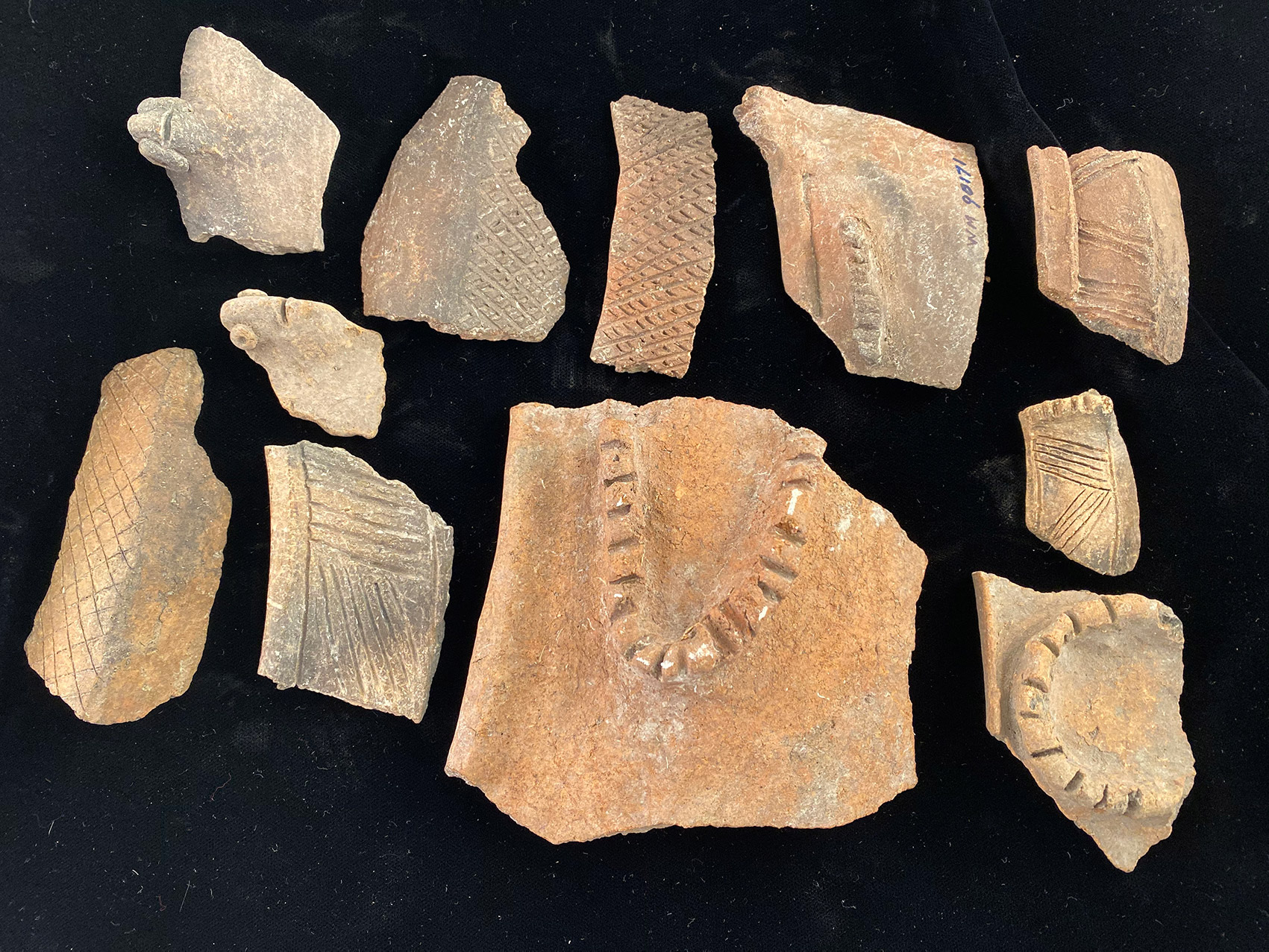 Broken pieces of reddish-orange pottery with different etchings and markings on them sit on a black background