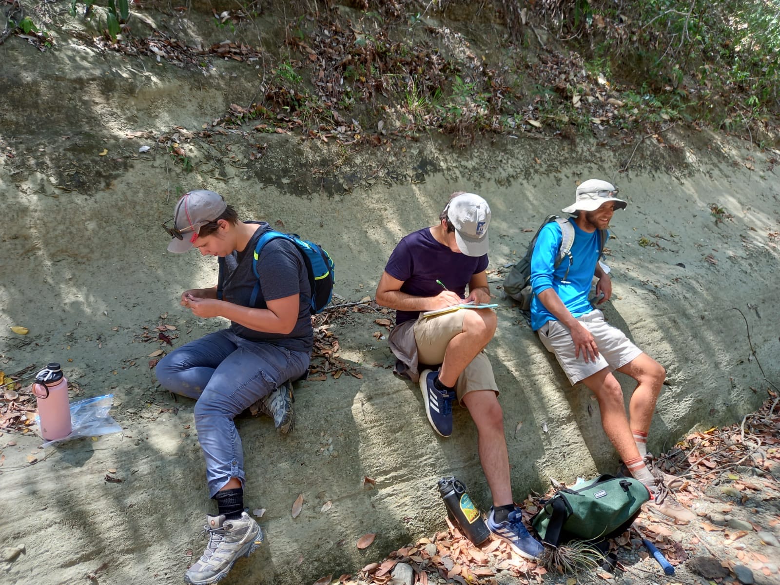Graduate students Carmi Milagros Thompson, Lazaro Viñola Lopez and Mitchell Riegler rest on a rock face to check notes and observe fossils at a field site in the Dominican Republic