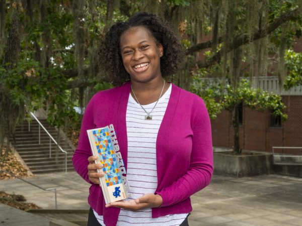 Adania Flemming stands against a background of oak and magnolia trees holding the UF Alumni Association Leadership award plaque