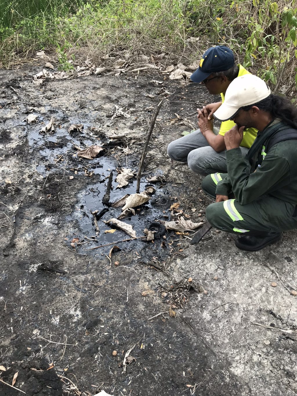 Two individuals inspect an open asphalt seep