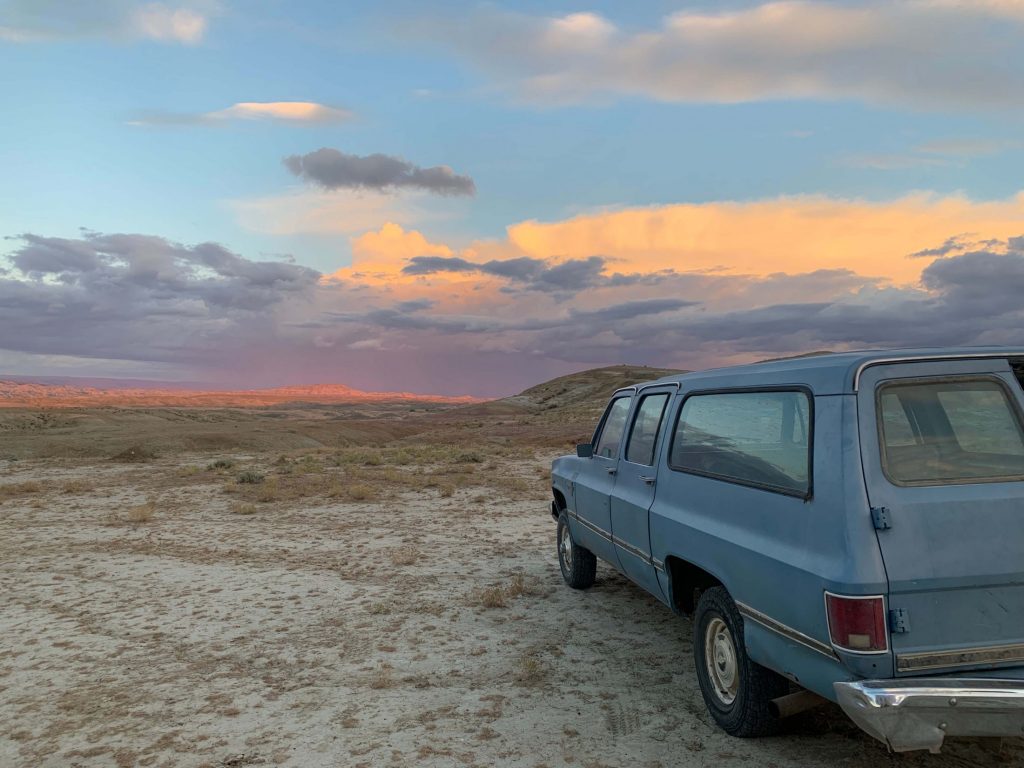 Old suburban car parked on sand overlooking a sunset