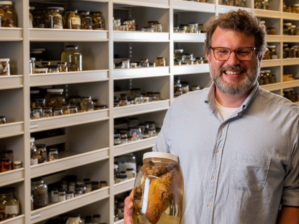 Man leans against a specimen shelf in a museum storeroom