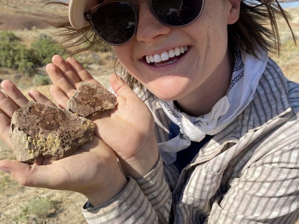 Woman poses in a desert, holding one plant fossil in each hand
