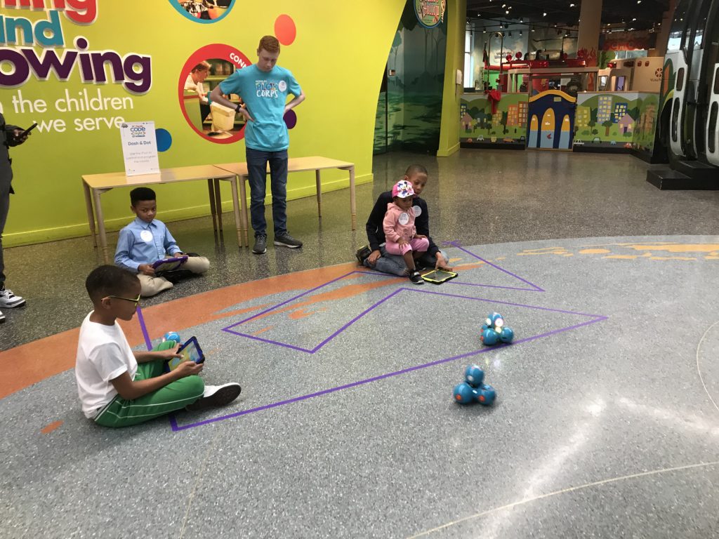 Children sit on the floor and play with remote controlled toys.