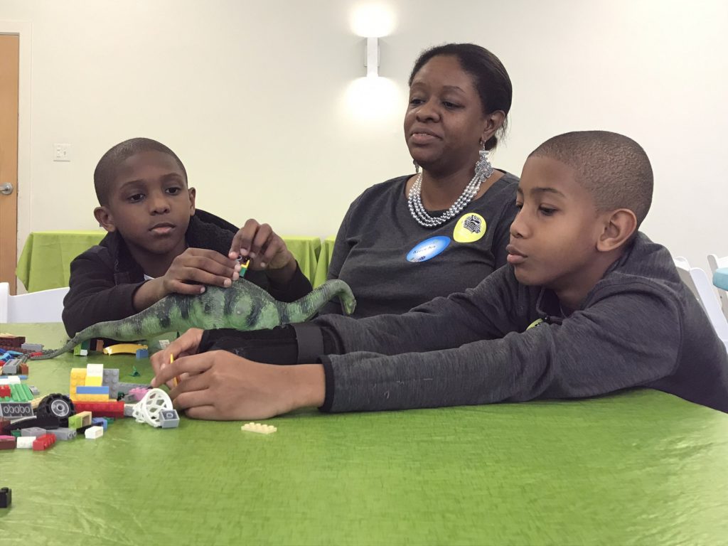 One adult and two children seated at a green table