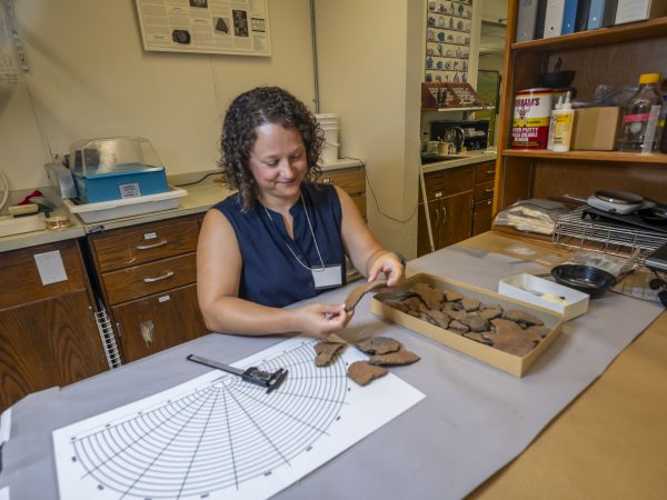 Andrea Torvinen sits at a desk in the Ceramic Technology Laboratory and examines pottery fragments.